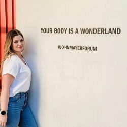 Kara standing in front of wall "Your Body Is a Wonderland".